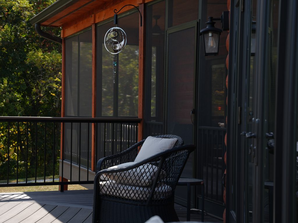 A picture of two chairs on the deck of a log home with screened-in porch in the background