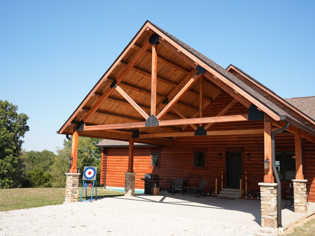 A picture of the porch of a log home with trees and the sky in the background