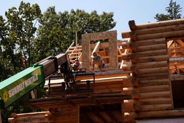 Men building a log home with a lift in the foreground