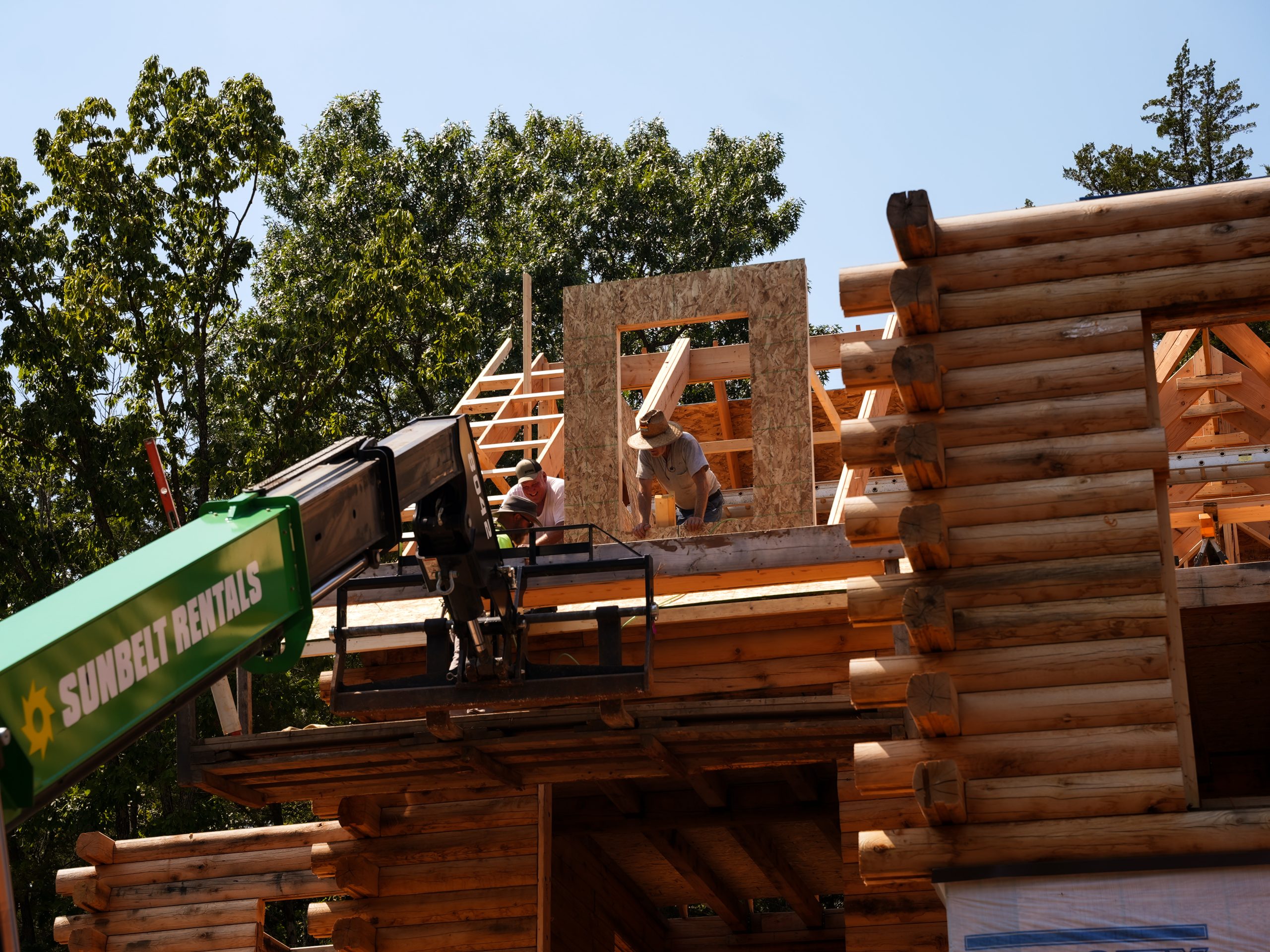 Men building a log home with a lift in the foreground