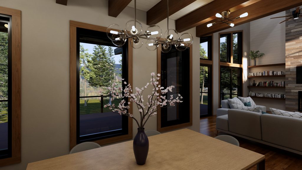 Modern mountain home dining area with a light wood table and flowering branch centerpiece, surrounded by large wood-trimmed windows overlooking a forested landscape; a contemporary chandelier hangs above, with the living room and built-in bookshelves visible beyond.