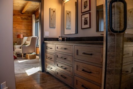 Bathroom wood cabinet counter and sinks, two pictures of children self portraits in black and white and a stretch canvass of Madison River Montana's topography.