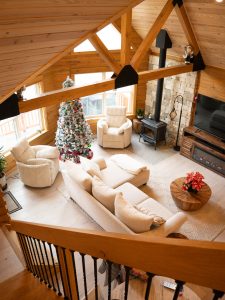 A picture of the living room of a log home with ceiling, furniture, fireplace and Christmas tree