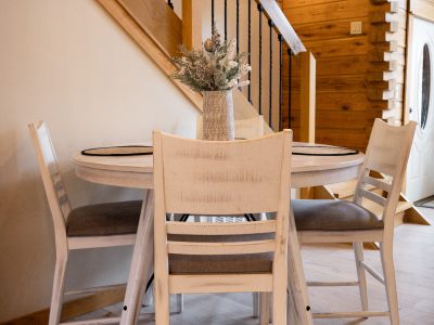 A picture of a white dining room table with four chairs and a vase of decorative flowers on top with a stairwell behind it